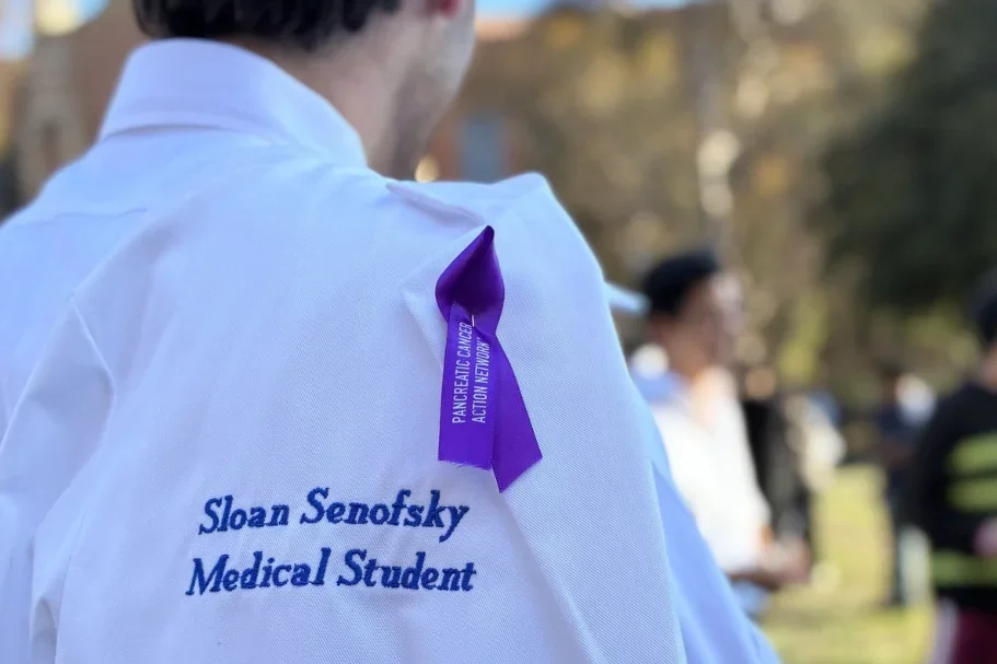 A purple pancreatic cancer awareness ribbon pinned to Sloan Senofsky’s white coat at his White Coat Ceremony